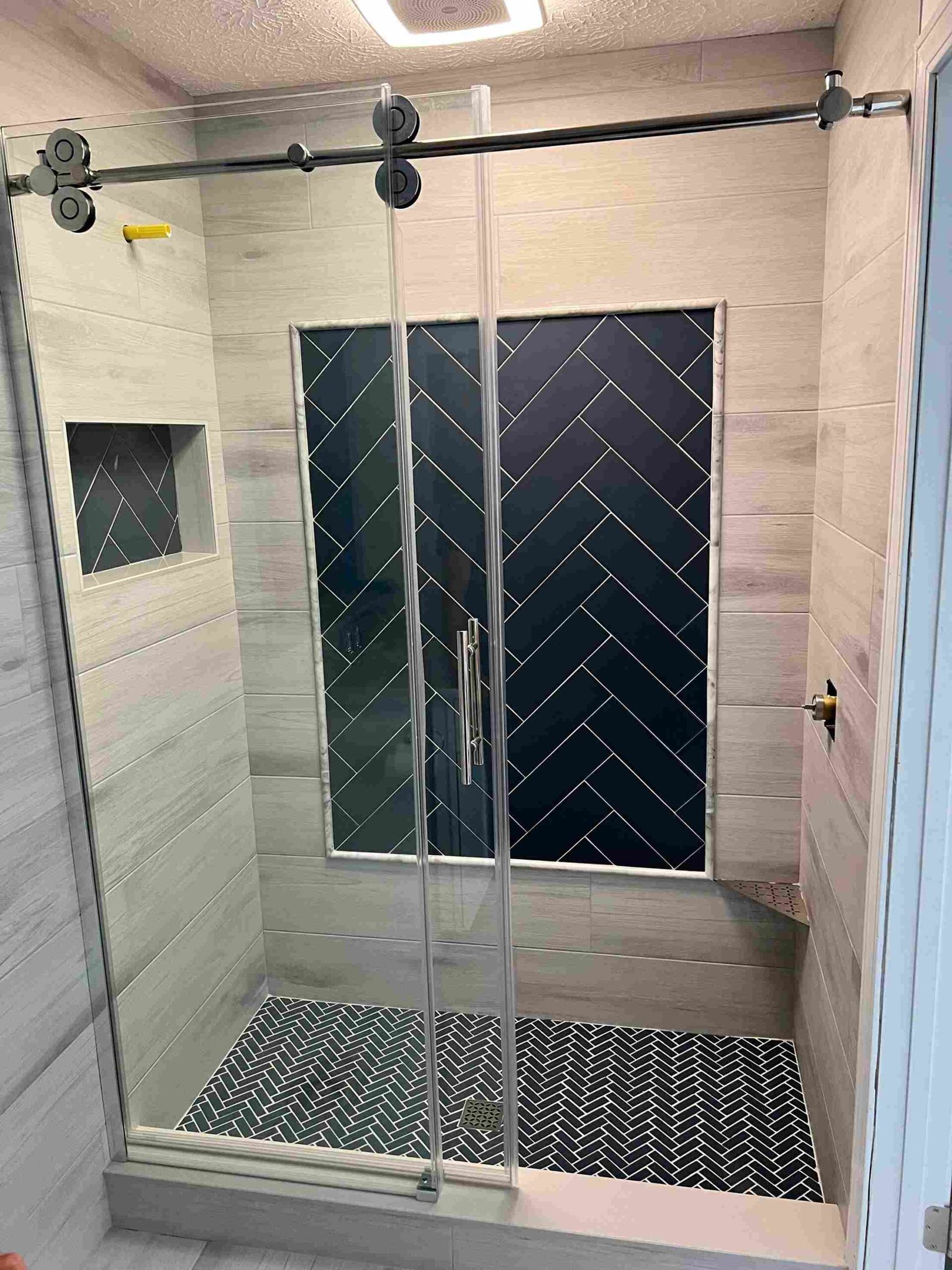 Custom walk-in shower with wood-look tile walls, navy herringbone feature wall and floor, and frameless glass door by Barys Tile in Panama City Beach